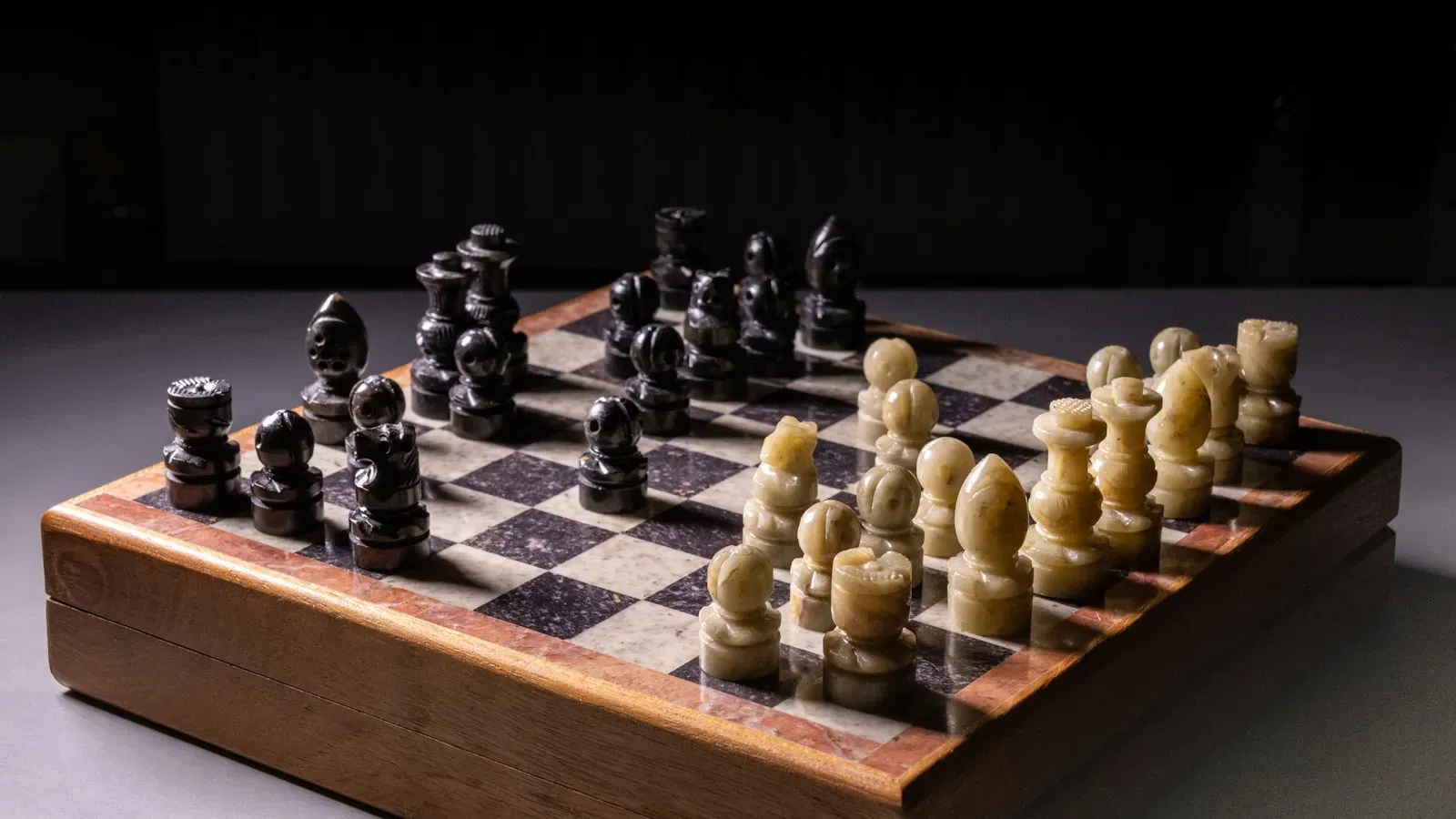 A marble chess set mid-game in dramatic light (photo by Kevin Hessey on Unsplash)