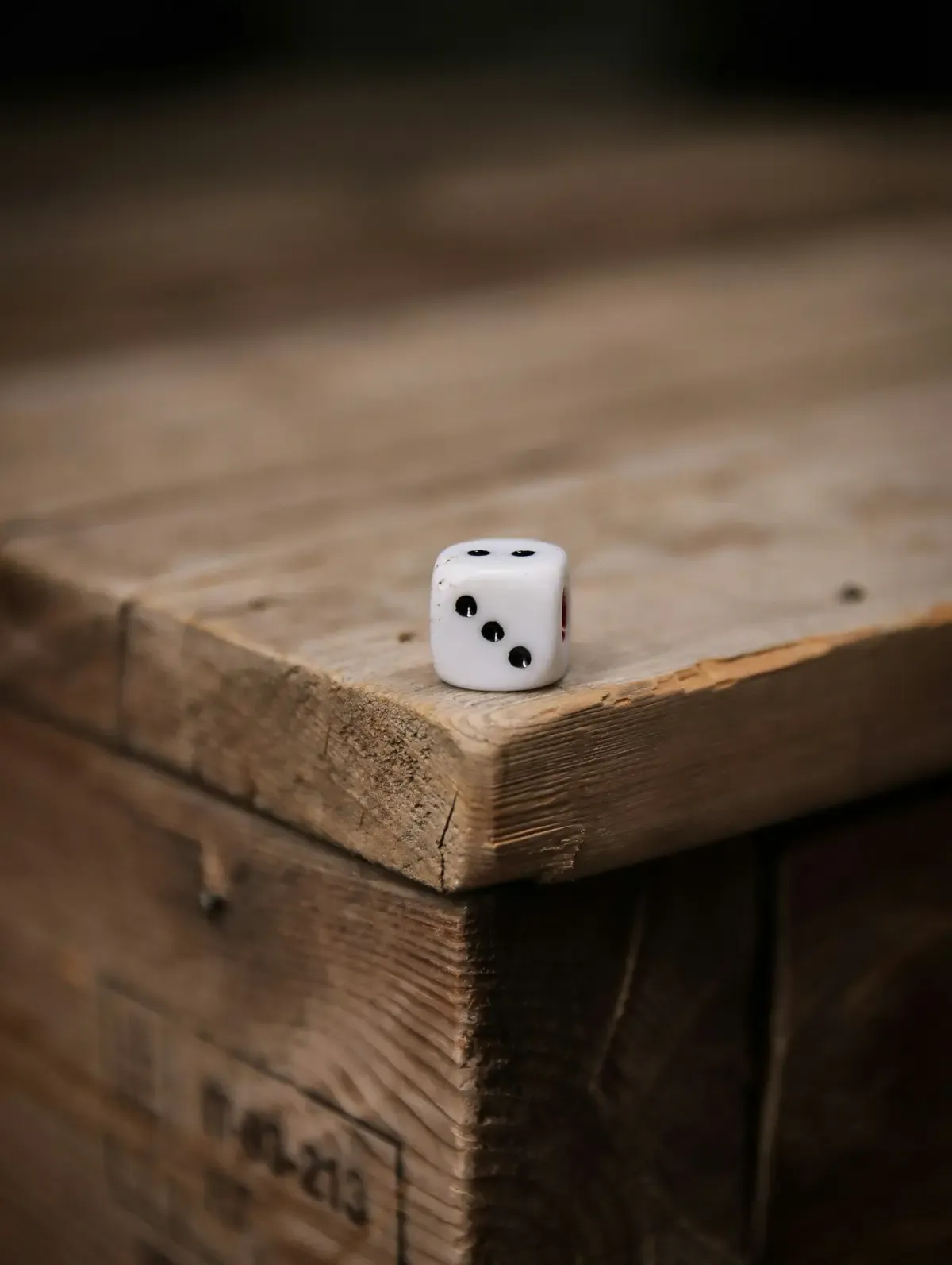 A single die resting on the corner of a wooden crate (photo by Zhuo Cheng you on Unsplash)