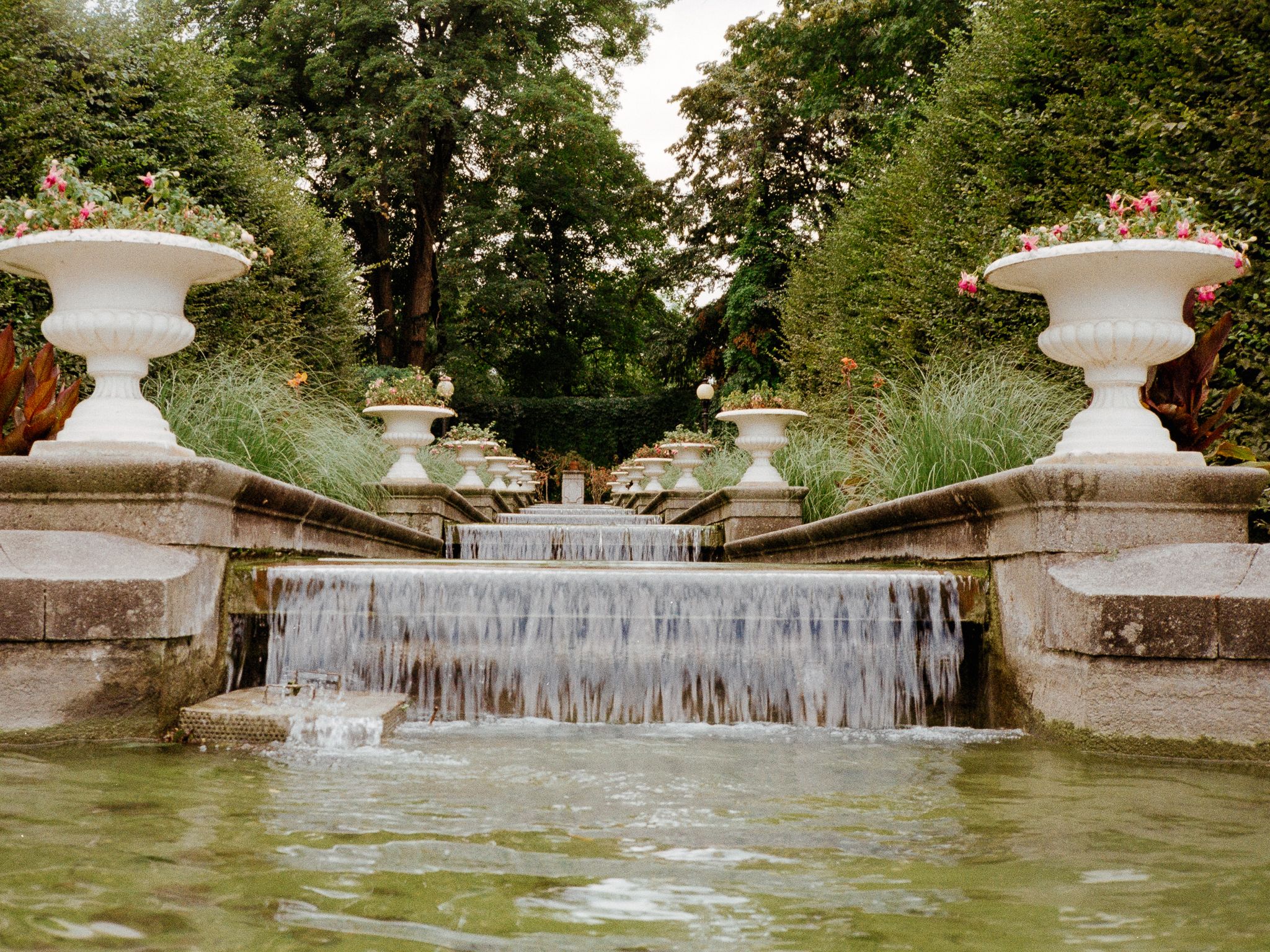 A stepped garden cascade flanked by white flower urns, spilling into a pool