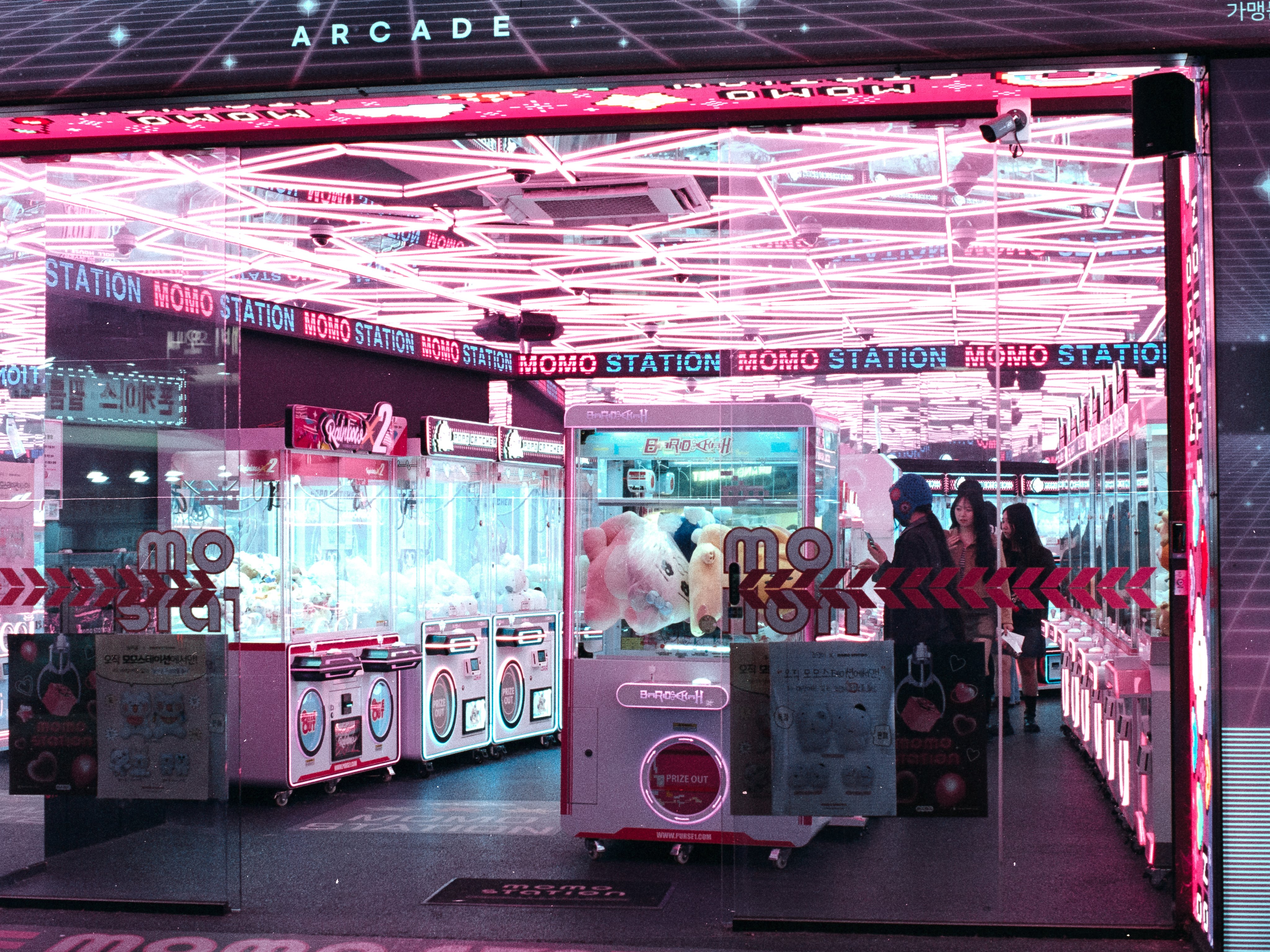 A claw machine arcade bathed in pink neon, mirrored ceiling and LED signs glowing