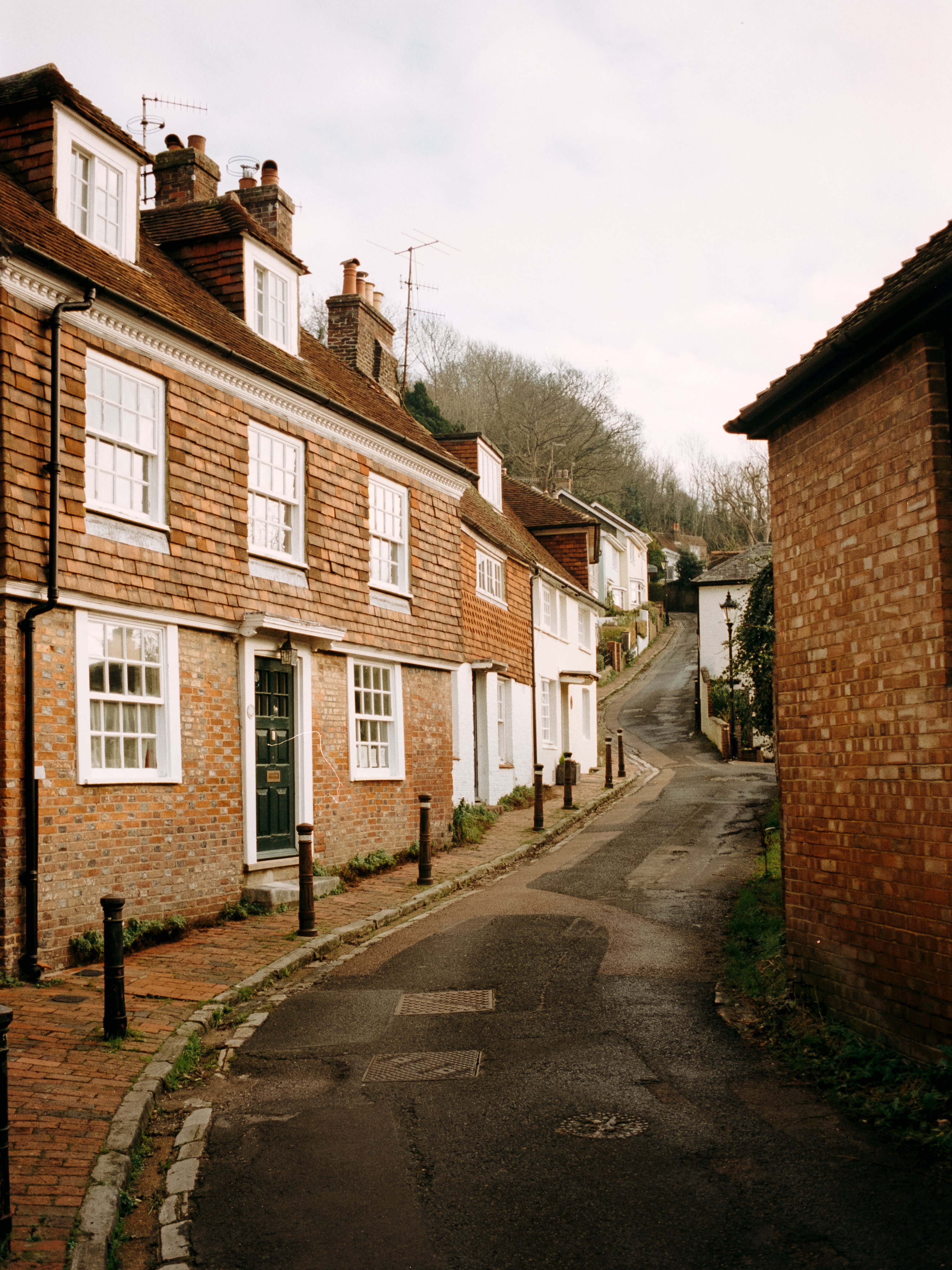 A narrow lane winding uphill between tile-hung brick cottages