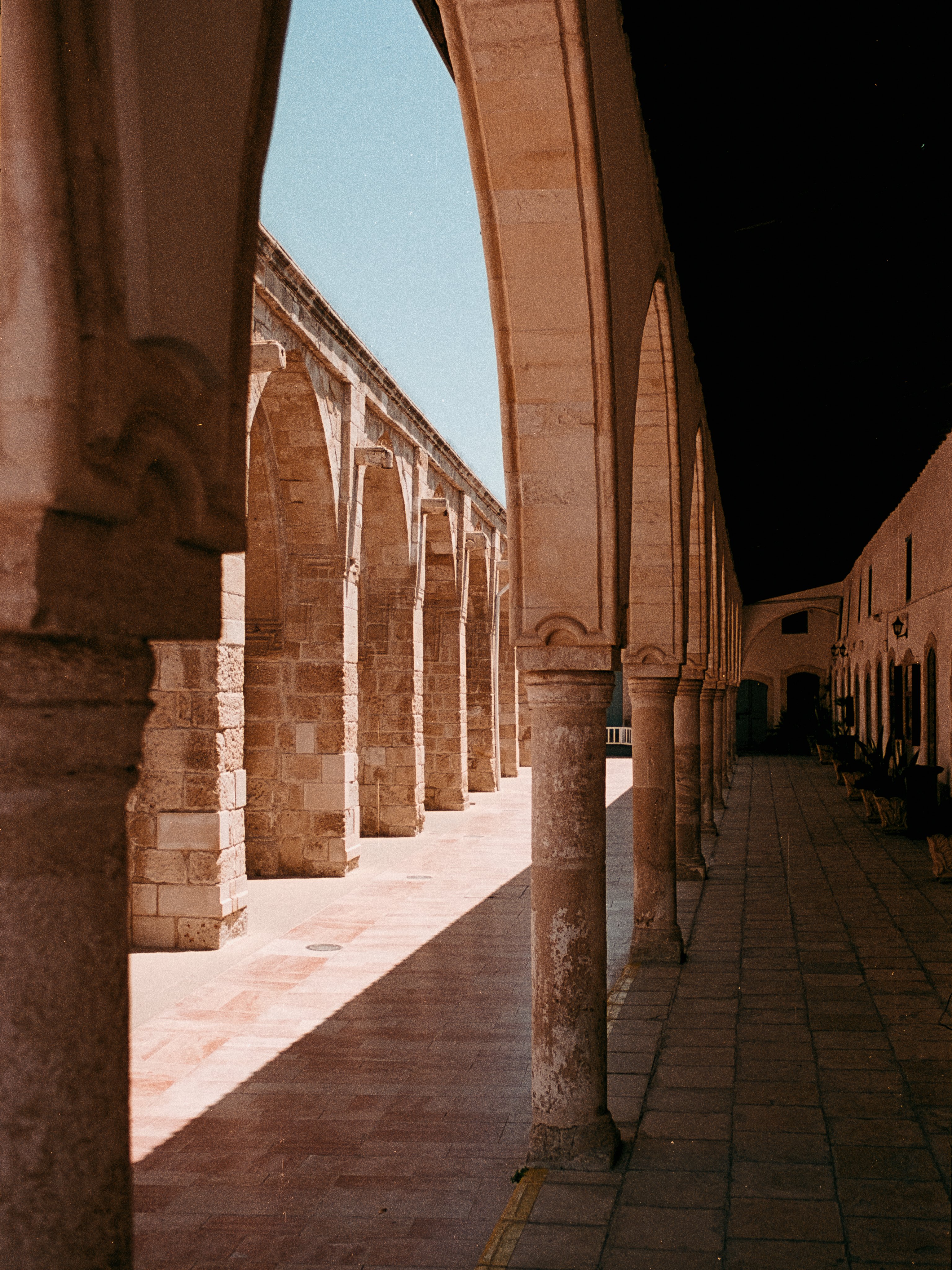 A sunlit stone arcade of pointed arches resting on slender columns