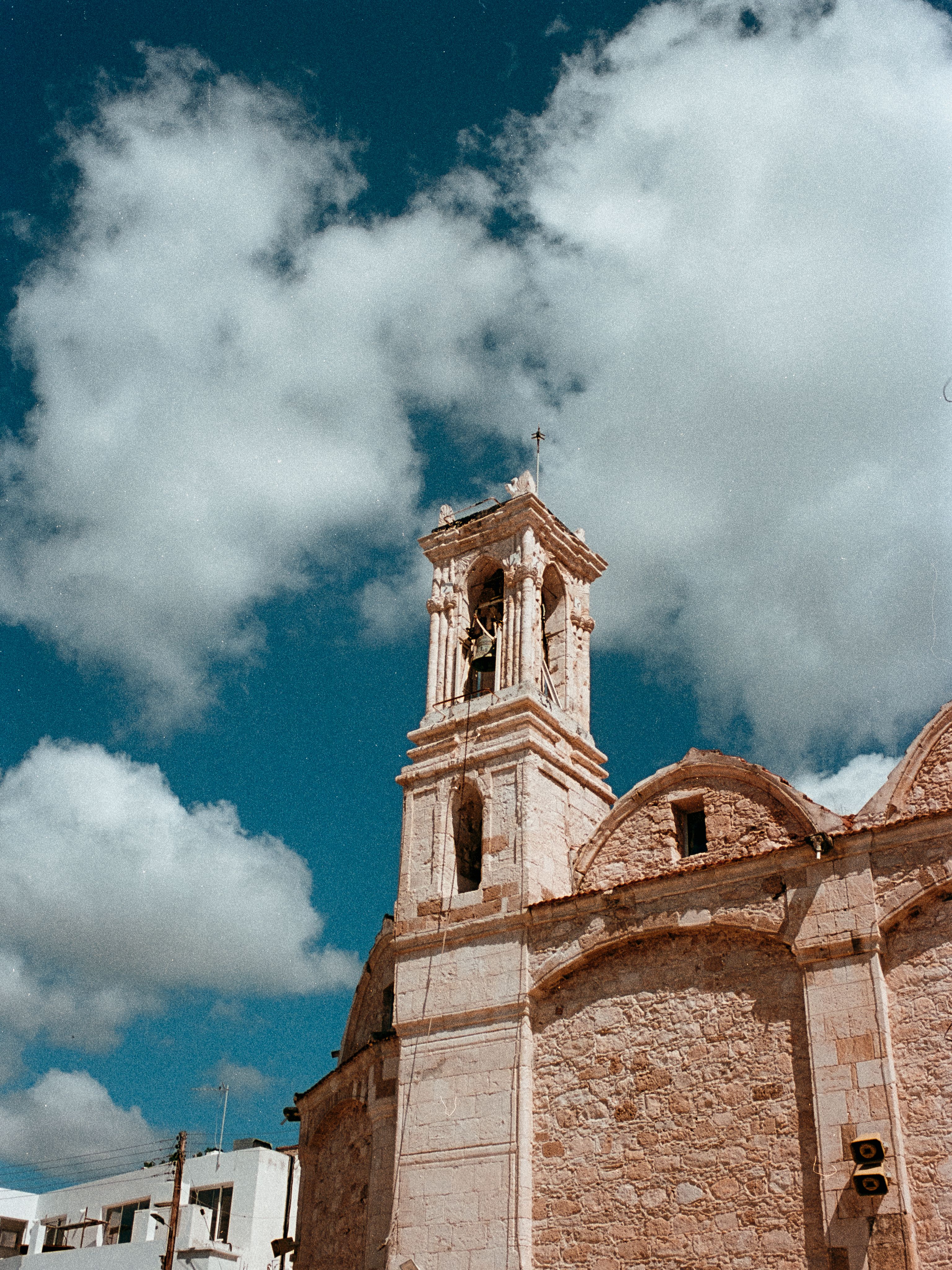 The bell tower of a stone church rising into a deep blue sky dotted with clouds