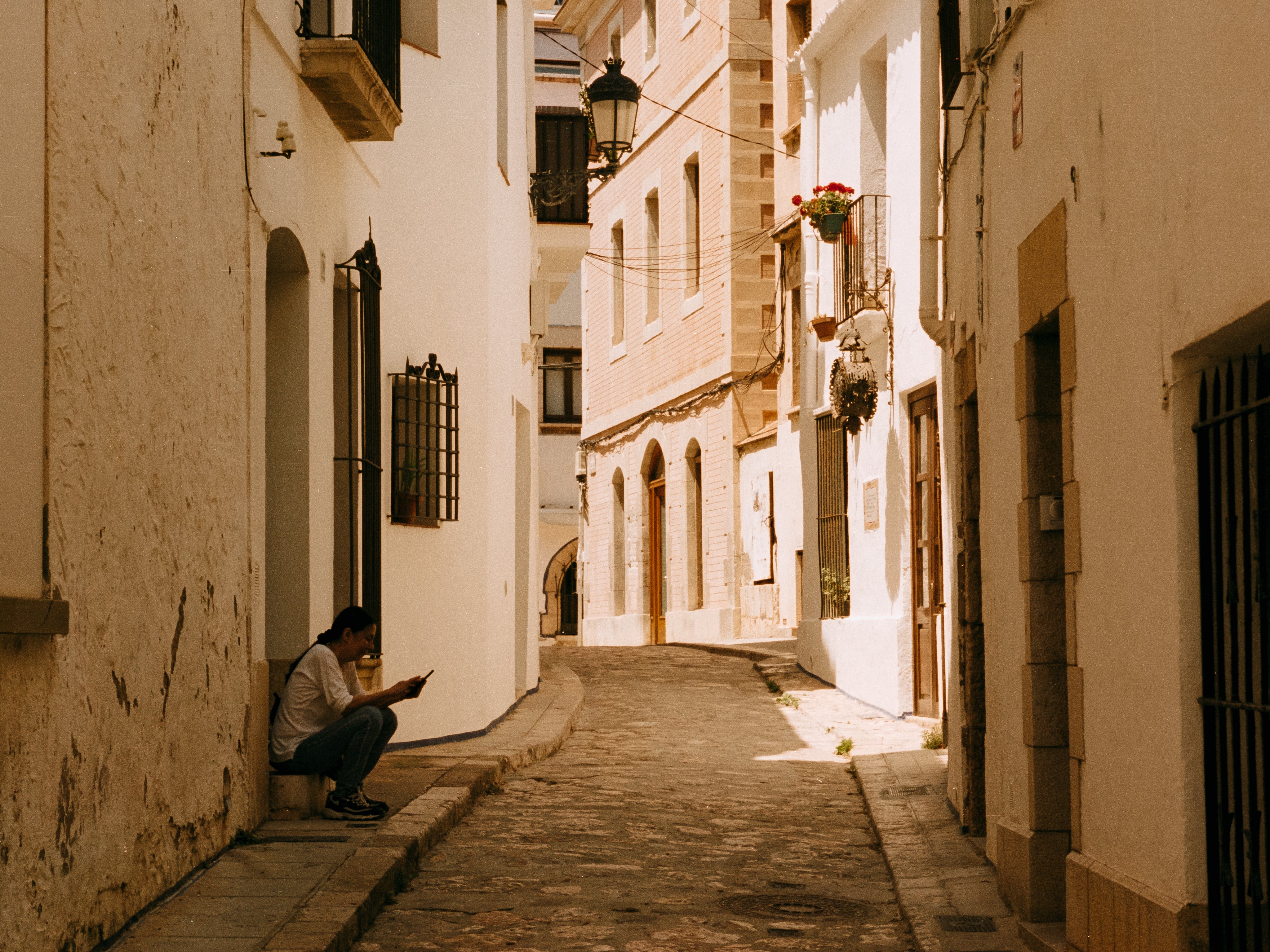 A woman on a doorstep checking her phone in a whitewashed cobbled alley