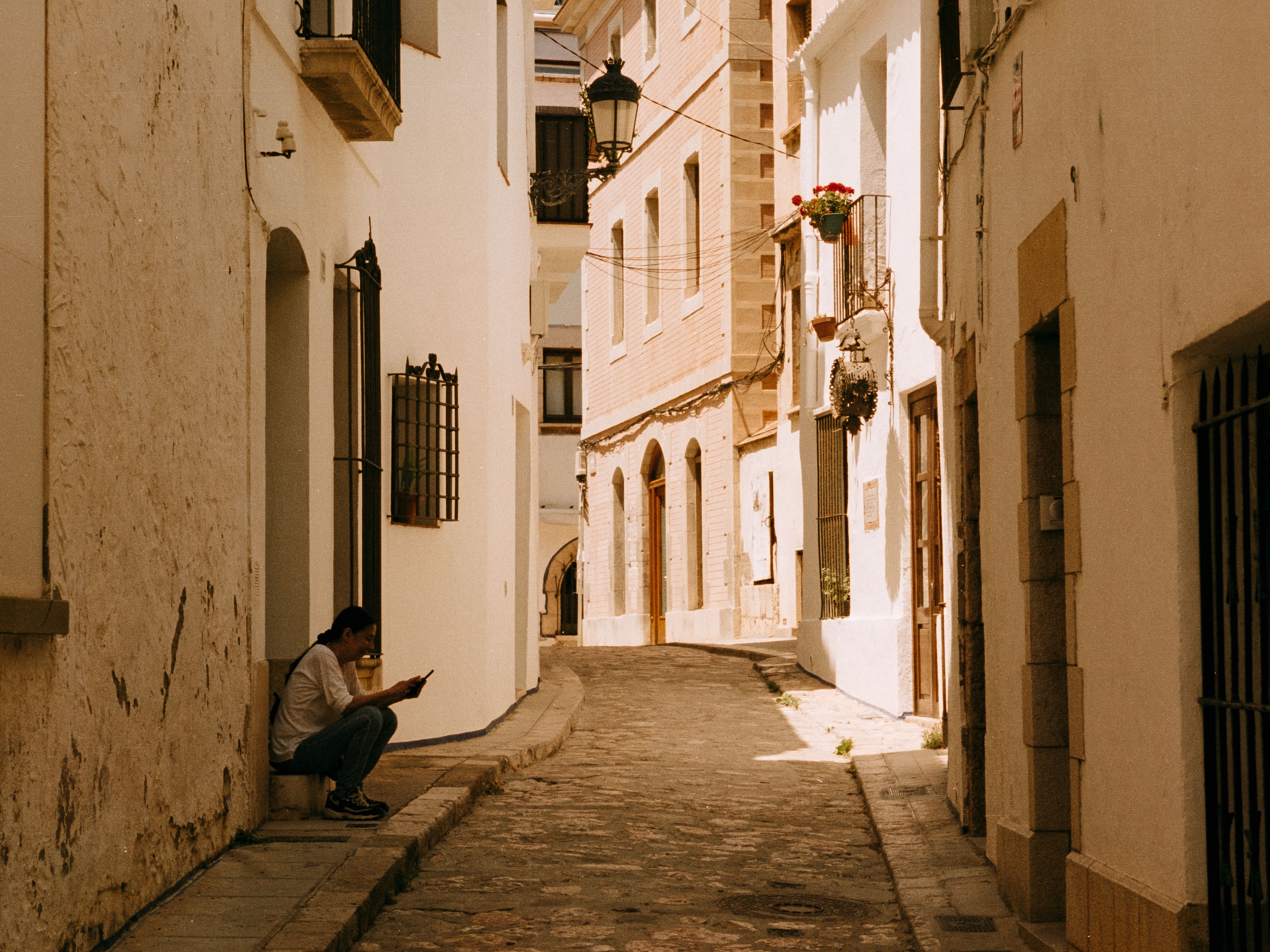 A woman on a doorstep checking her phone in a whitewashed cobbled alley